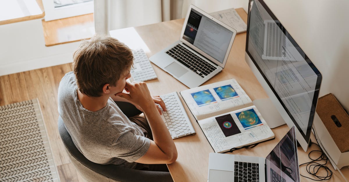 Top view of young programmer working on multiple laptops in a modern office setting.